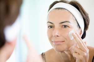 Woman applying face cream in front of mirror